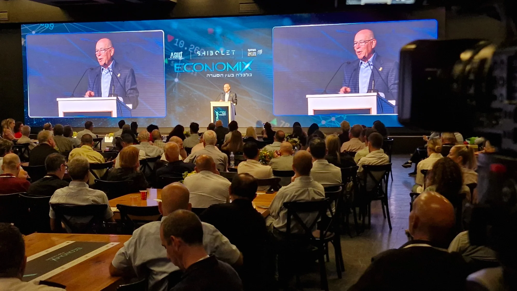 שידור וידאו במעגל סגור בכנס עם מרצה על הבמה ומסכים באולם